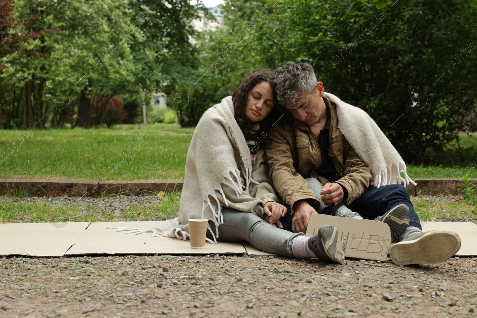 Photo of Poor people with sign Homeless and paper cup on carton in park, space for text