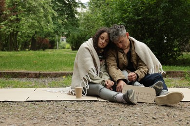 Photo of Poor people with sign Homeless and paper cup on carton in park, space for text