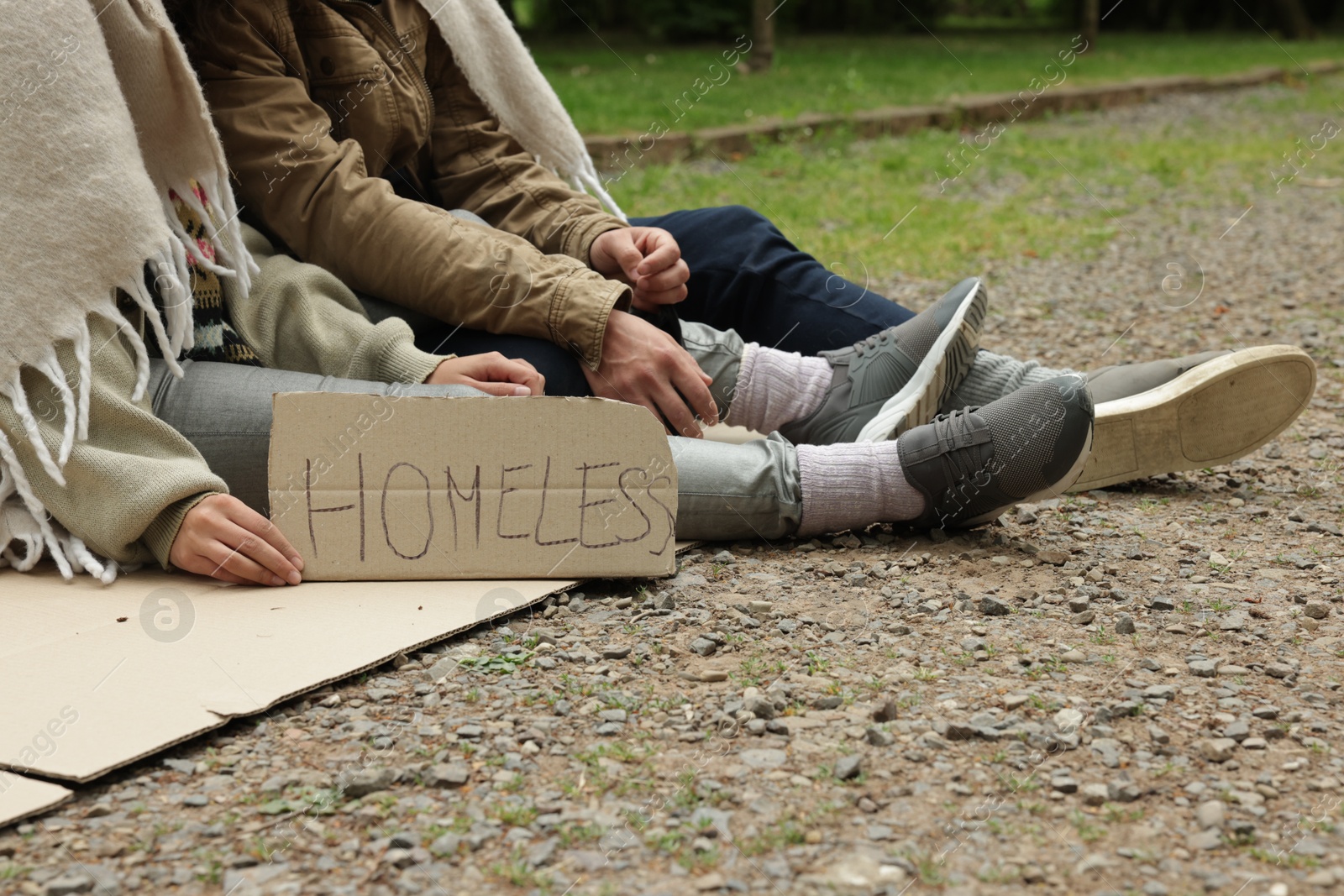 Photo of Poor people with sign Homeless on carton in park, closeup