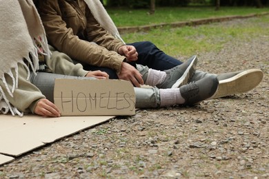 Photo of Poor people with sign Homeless on carton in park, closeup
