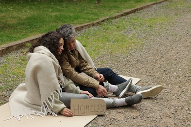Photo of Poor people with sign Homeless on carton in park