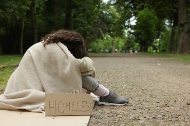 Photo of Poor woman with sign Homeless on carton in park, space for text