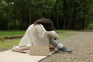 Photo of Poor woman with sign Homeless on carton in park