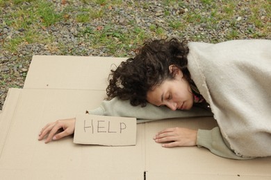 Photo of Homeless woman with sign Help sleeping on carton in park