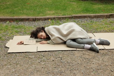 Photo of Homeless woman with sign Help sleeping on carton in park