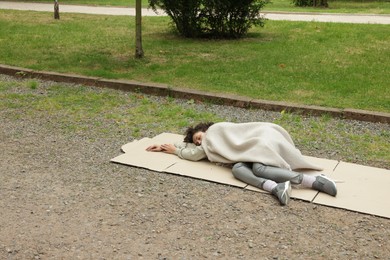 Photo of Homeless woman sleeping on carton in park, space for text