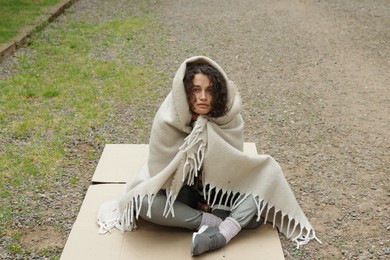 Photo of Homeless woman wrapped with blanket on carton in park