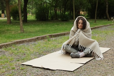 Photo of Homeless woman wrapped with blanket on carton in park, space for text