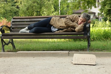 Photo of Poor man sleeping on bench and sign Homeless in park