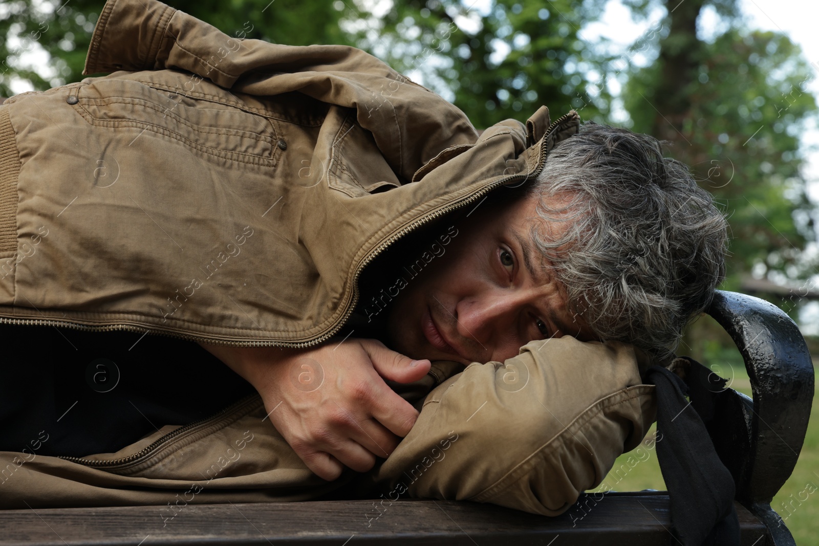 Homeless man lying on bench in park Photo of Homeless man lying on bench in park