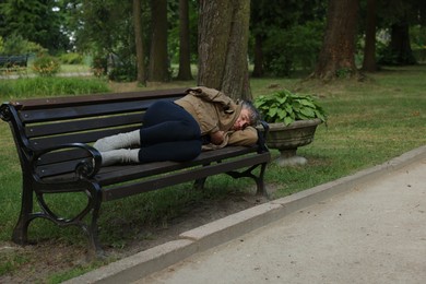 Photo of Homeless man sleeping on bench in park, space for text