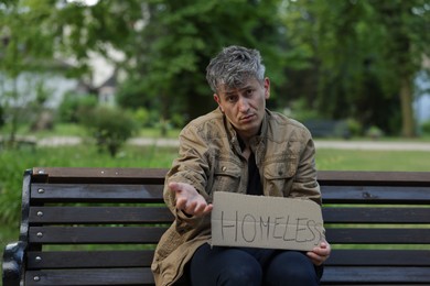 Photo of Poor man with sign Homeless begging for money on bench in park