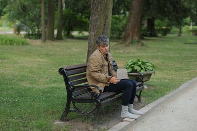 Photo of Poor man with sign Homeless on bench in park