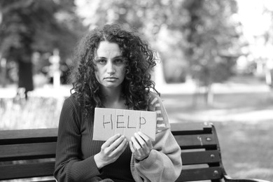 Photo of Homeless woman with sign Help on bench in park, space for text. Black and white effect