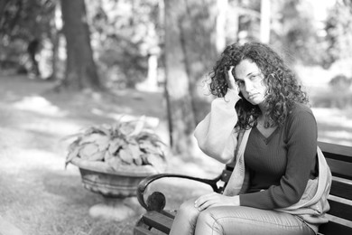 Photo of Homeless woman on bench in park, space for text. Black and white effect