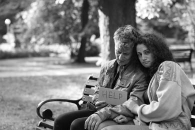 Photo of Homeless people with sign Help on bench in park, space for text. Black and white effect
