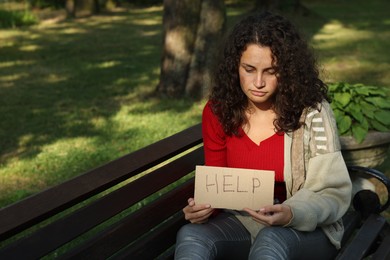 Photo of Homeless woman with sign Help on bench in park