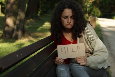 Photo of Homeless woman with sign Help on bench in park