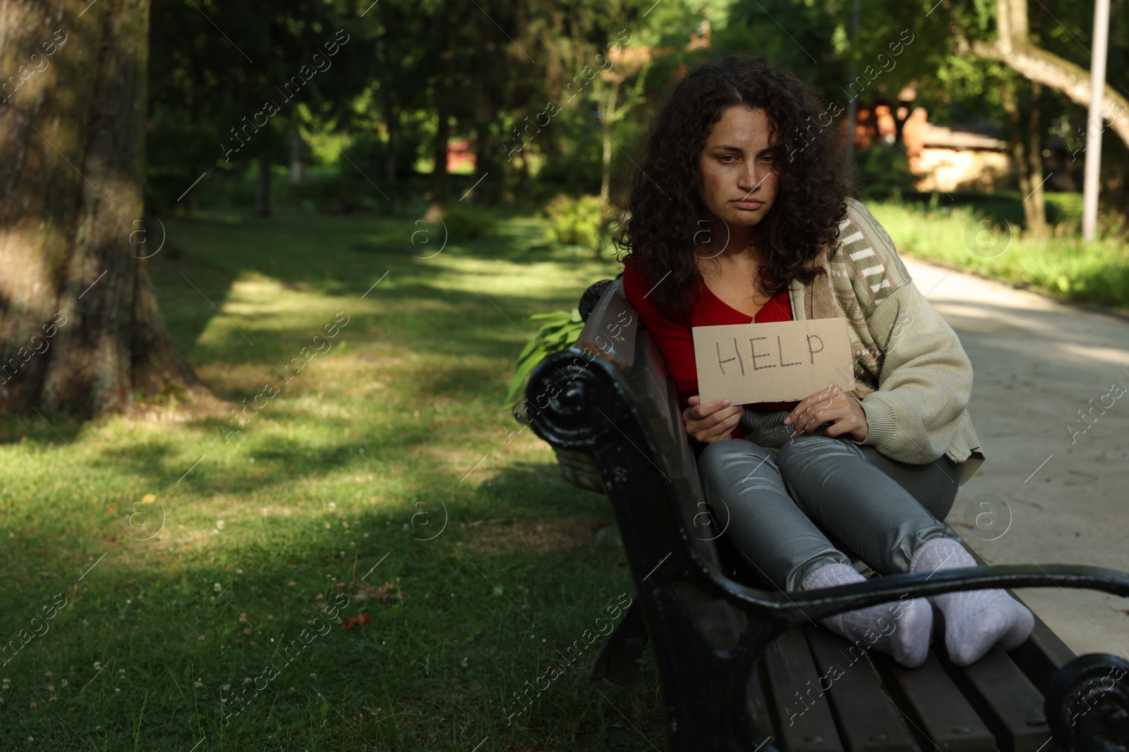 Homeless woman with sign Help on bench in park, space for text Photo of Homeless woman with sign Help on bench in park, space for text