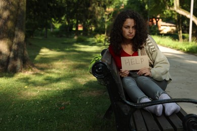 Photo of Homeless woman with sign Help on bench in park, space for text