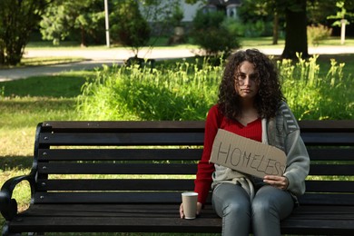 Photo of Poor woman with sign Homeless and paper cup on bench in park