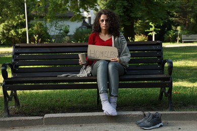 Photo of Poor woman with sign Homeless and paper cup on bench in park
