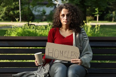 Photo of Poor woman with sign Homeless and paper cup on bench in park