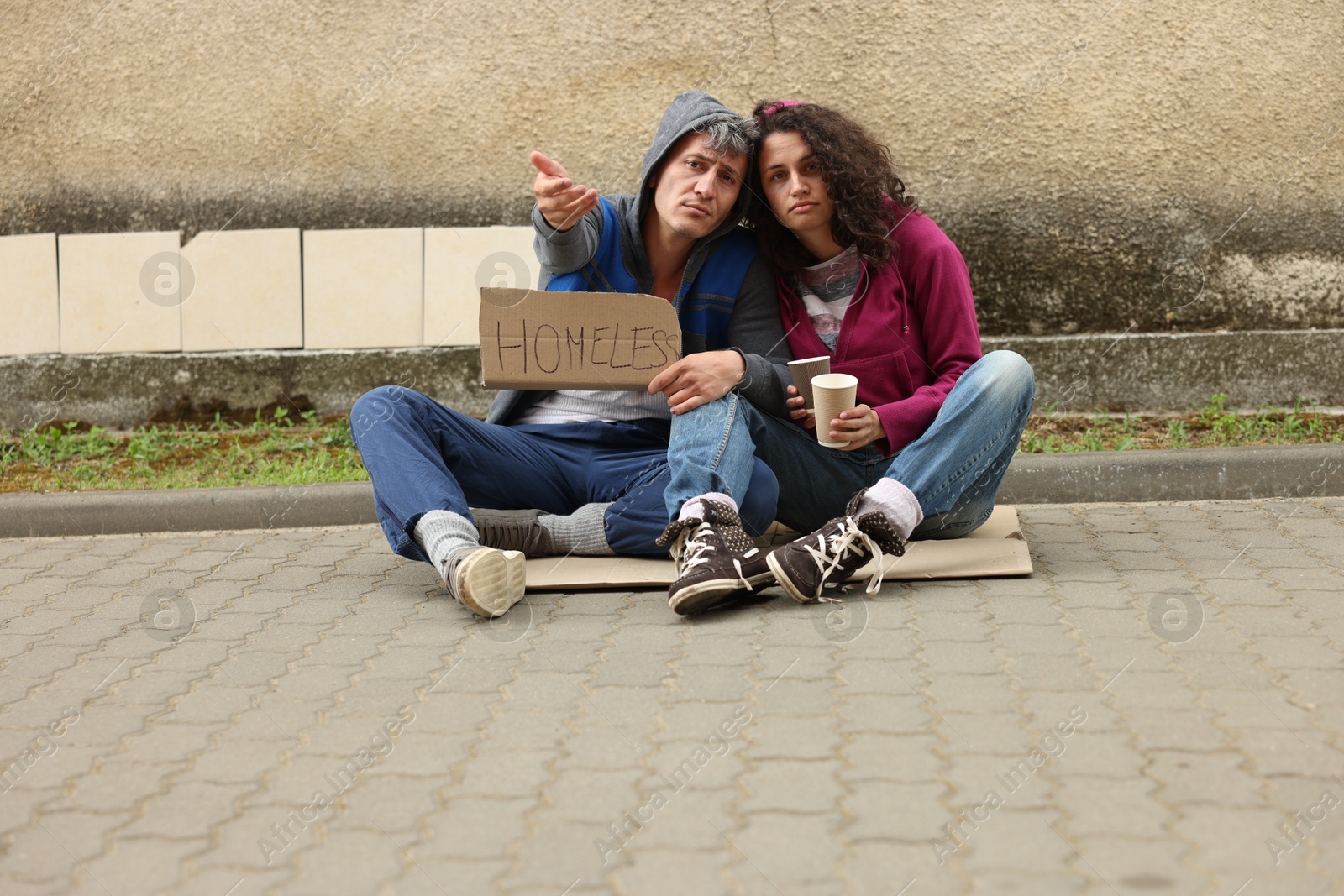 Poor people with sign Homeless and paper cups begging for money on carton outdoors Photo of Poor people with sign Homeless and paper cups begging for money on carton outdoors