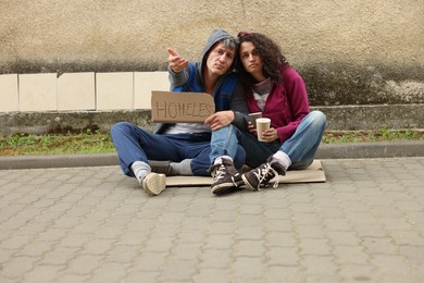 Photo of Poor people with sign Homeless and paper cups begging for money on carton outdoors