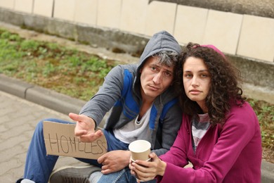 Photo of Poor people with sign Homeless and paper cups begging for money outdoors