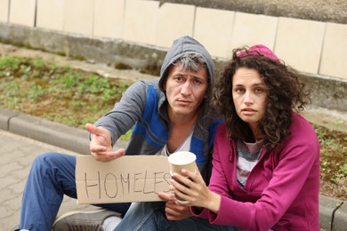 Photo of Poor people with sign Homeless and paper cups begging for money outdoors