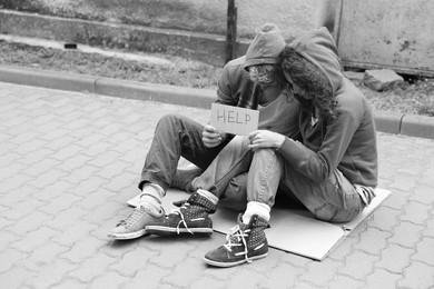 Photo of Homeless people with sign Help on carton outdoors, space for text. Black and white effect