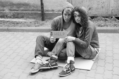 Photo of Homeless people with sign Help on carton outdoors. Black and white effect