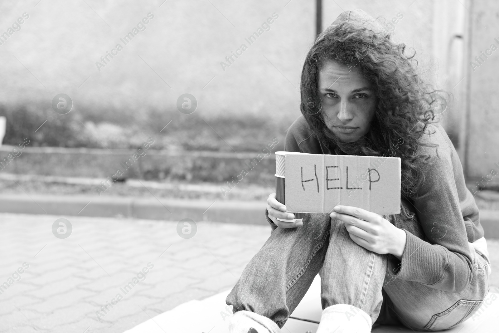 Homeless woman with sign Help and paper cups on carton outdoors, space for text. Black and white effect Photo of Homeless woman with sign Help and paper cups on carton outdoors, space for text. Black and white effect