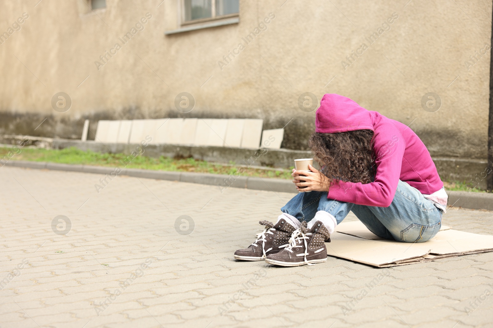 Homeless woman with paper cups on carton outdoors, space for text Photo of Homeless woman with paper cups on carton outdoors, space for text