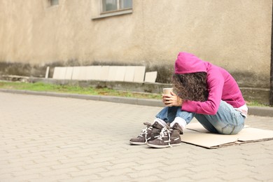 Photo of Homeless woman with paper cups on carton outdoors, space for text