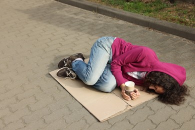 Photo of Homeless woman with paper cups lying on carton outdoors
