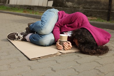 Photo of Homeless woman with paper cups lying on carton outdoors
