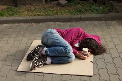 Photo of Homeless woman with paper cups lying on carton outdoors