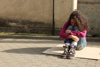 Photo of Homeless woman sitting on carton outdoors, space for text