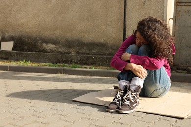 Photo of Homeless woman sitting on carton outdoors, space for text