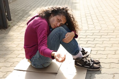 Photo of Homeless woman begging for money on carton outdoors