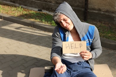Photo of Homeless man with sign Help begging for money on carton outdoors, space for text