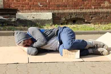Photo of Homeless man sleeping on carton and sign Help outdoors