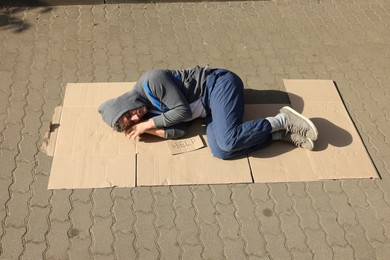 Photo of Homeless man sleeping on carton and sign Help outdoors