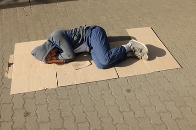 Photo of Homeless man sleeping on carton and sign Help outdoors