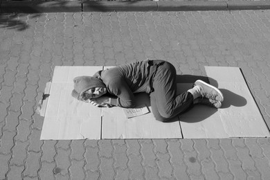 Photo of Homeless man sleeping on carton and sign Help outdoors. Black and white effect