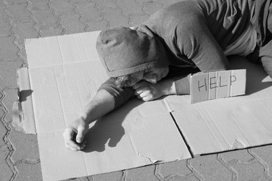 Photo of Homeless man sleeping on carton and sign Help outdoors. Black and white effect