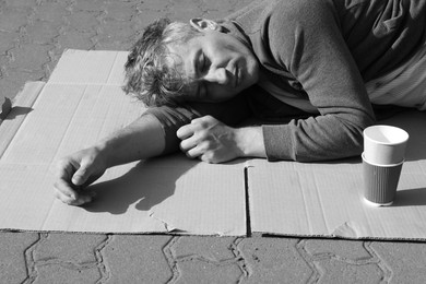 Photo of Homeless man sleeping on carton and paper cups outdoors. Black and white effect
