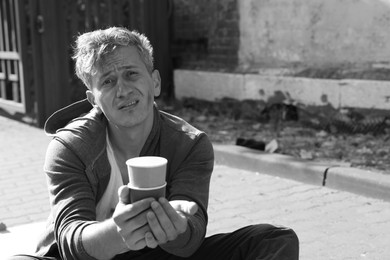 Photo of Homeless man with paper cups begging for money outdoors, space for text. Black and white effect